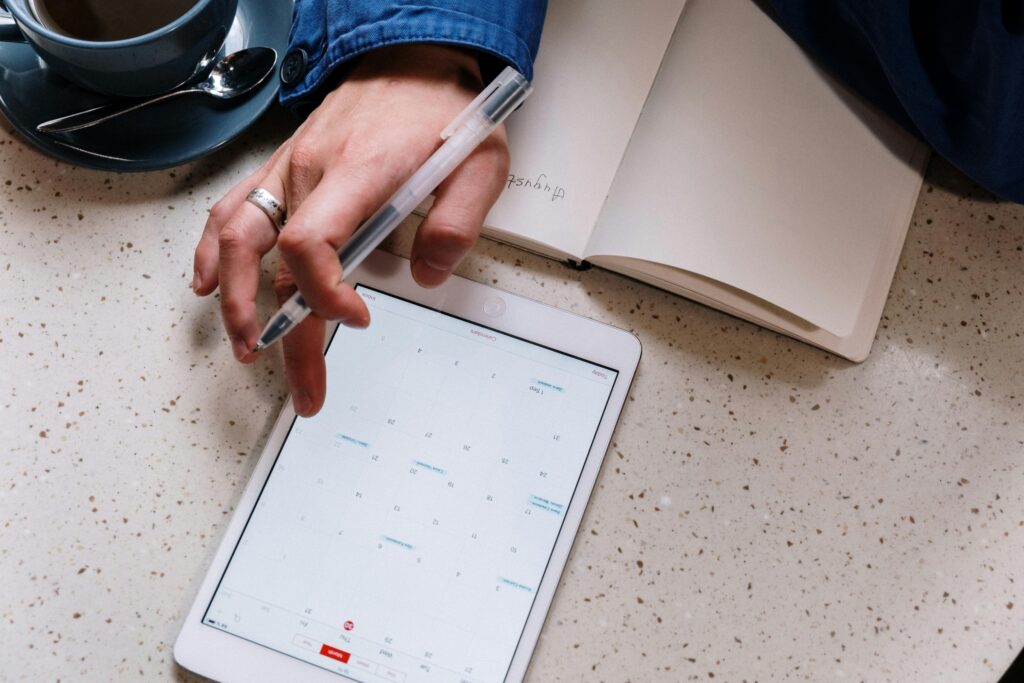 Person using a tablet for planning with an open notebook and coffee. Ideal for tech and productivity visuals.